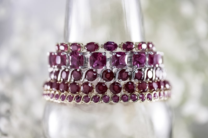 Five pinkish red ruby bracelets are shown stacked on top of each other against a white background.  