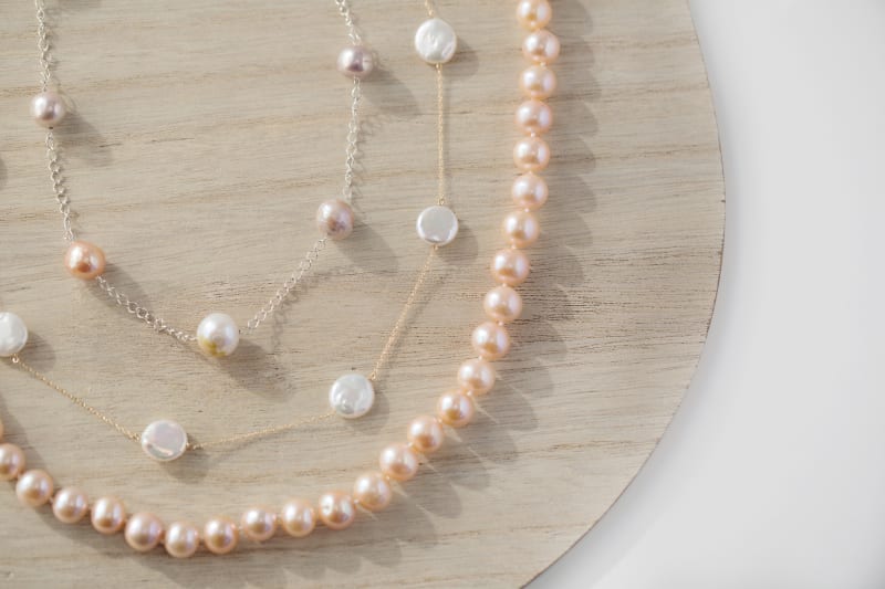 A multilayered necklace with pearls is shown posed against a round wood surface. 