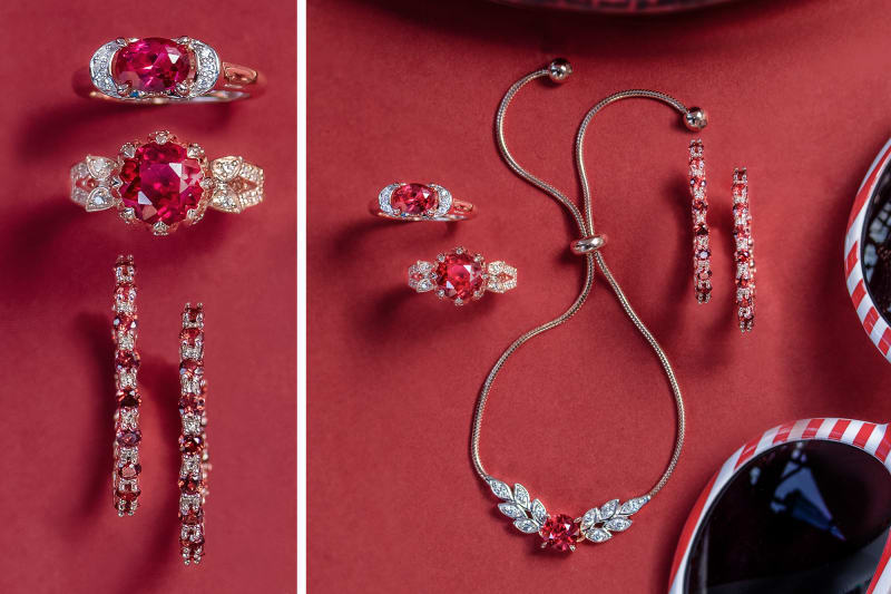 Ruby rings, necklaces, and earrings laid out on a red background with red and white striped sunglasses.  