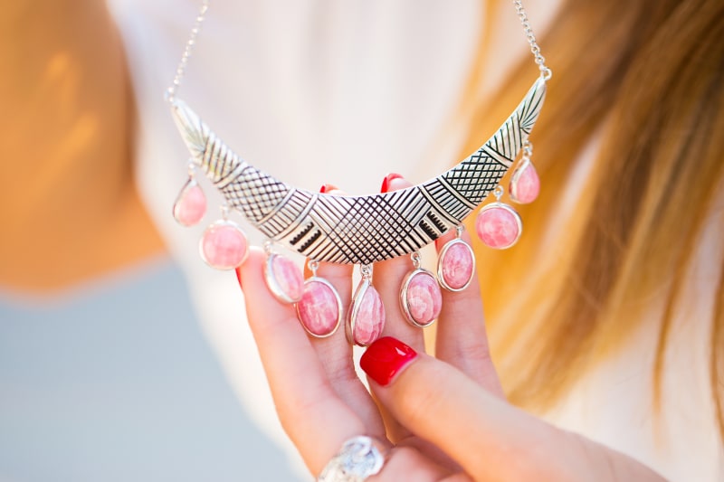 This is a product shot of a sterling silver necklace with pink, rhodochrosite stones hanging from the bottom. 
