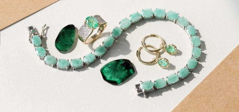 An emerald bracelet, ring, pair of earrings, and two loose gemstones are all pictured together. 