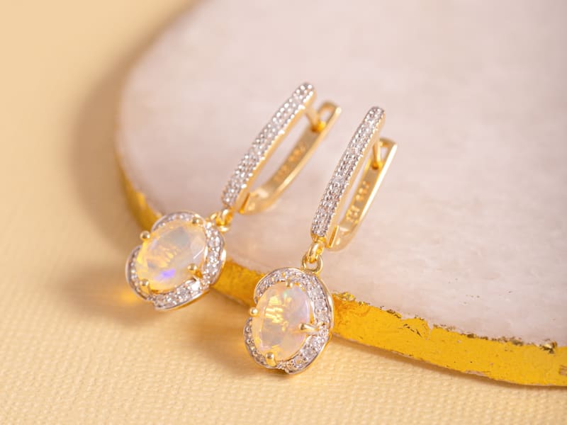 Close-up of white Ethiopian opal yellow gold dangle earrings. 