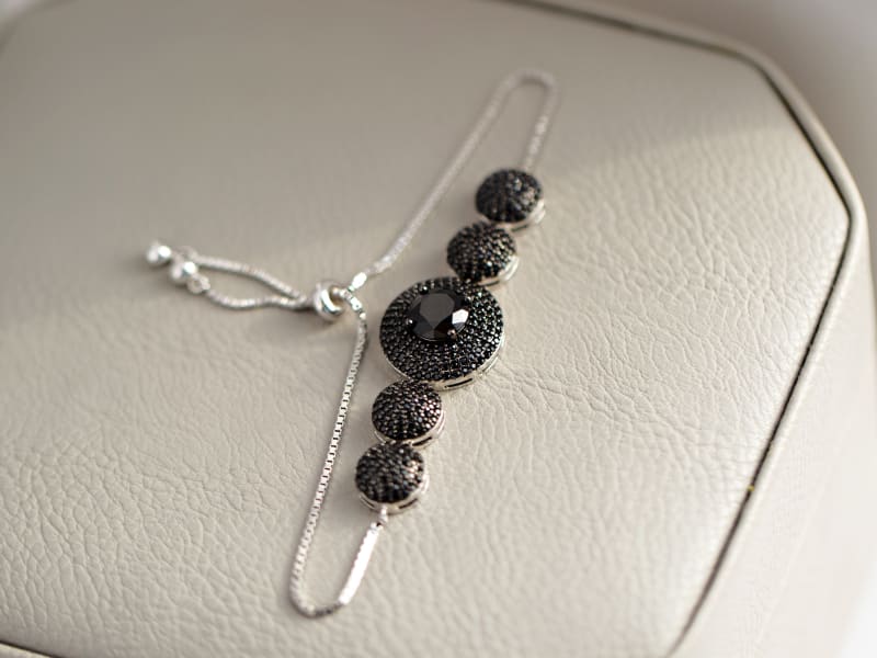 Photo of a dainty black spinel sterling silver bracelet. The bracelet is shot on a grey leather background.  