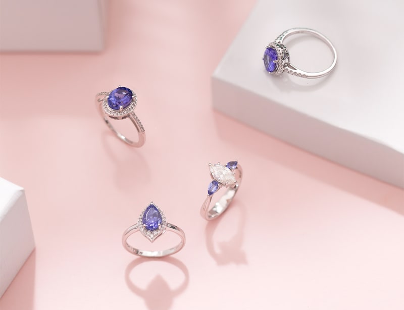 This photo includes four silver rings with purplish blue stones at the center of each, accented with smaller clear stones. 