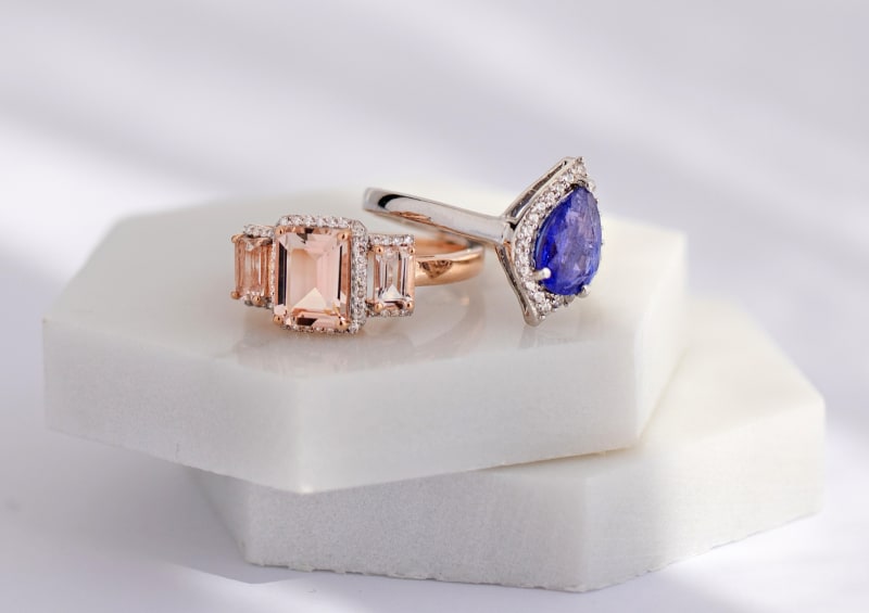 Two rings side by side. The first ring is a pink morganite ring with three gemstones, and the second ring is a blue tanzanite silver ring. 