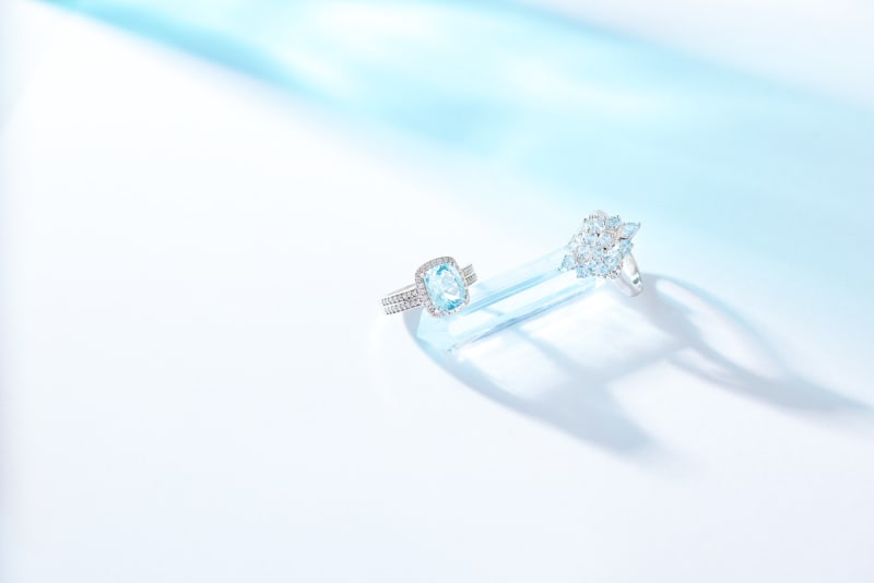 Two aquamarine, silver rings photographed on a light blue background, one has a bigger stone than the other. 