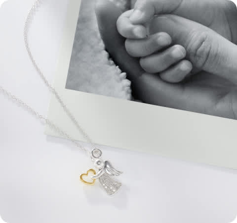 polaroid photo a baby holding an adults had with a kids angel pendant laying next to it