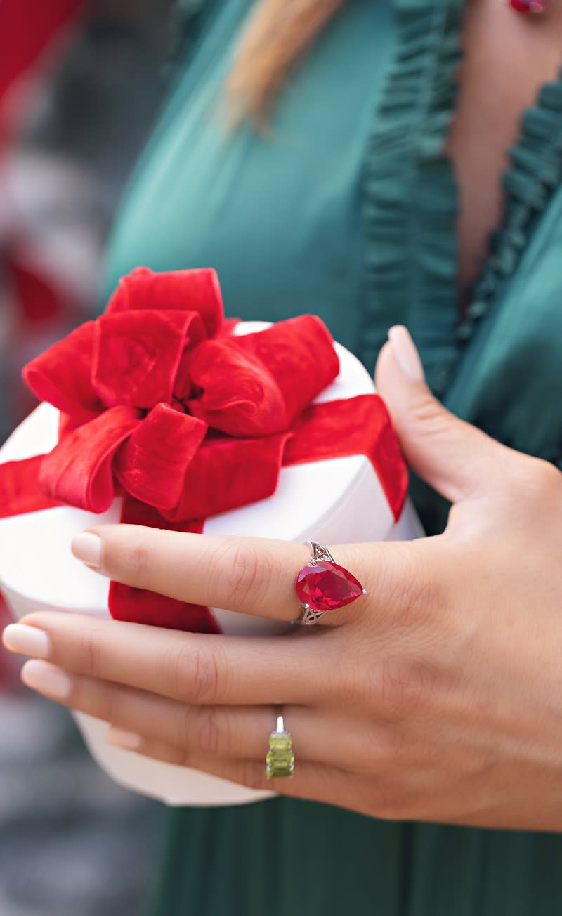 A hand adorned with silver red and green gemstone rings holding a present. 