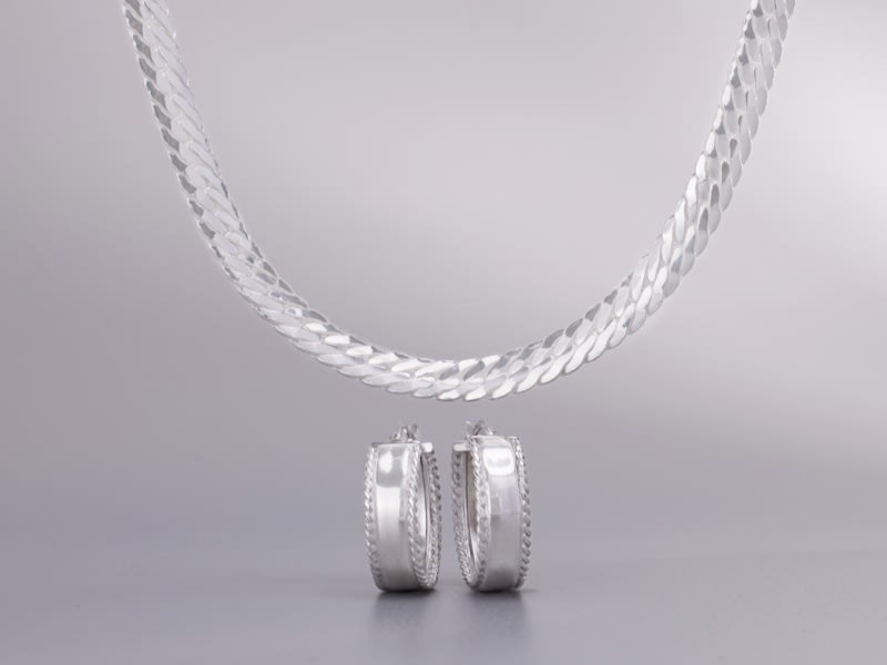 a thick silver necklace and two silver hoop earrings 