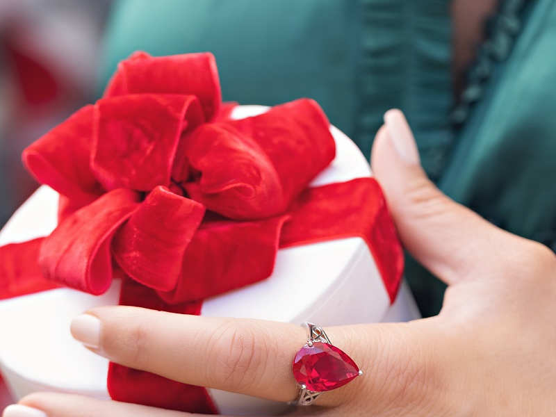 A hand adorned with silver red and green gemstone rings holding a present. 