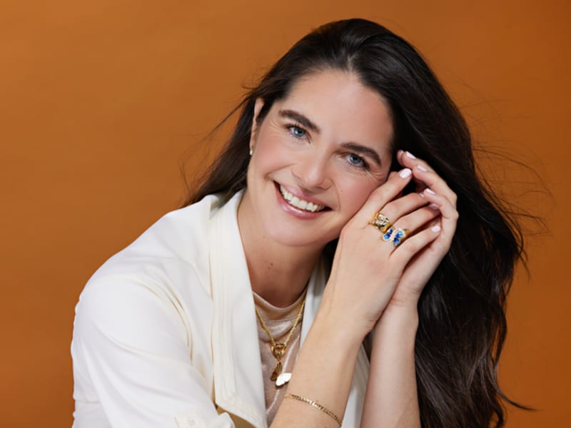A woman displays a fun and feminine gold necklace, bracelet and rings. 