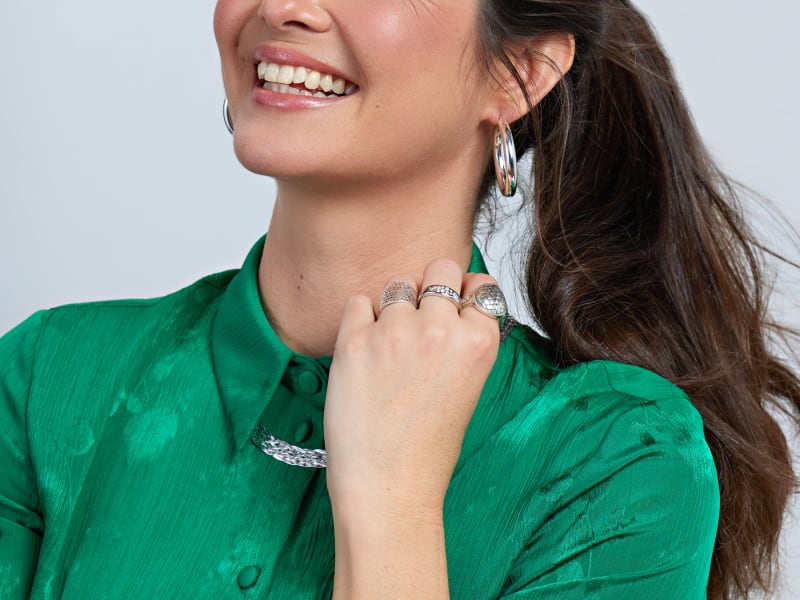A woman smiles while wearing stunning silver jewelry: a necklace, bracelet and rings. 