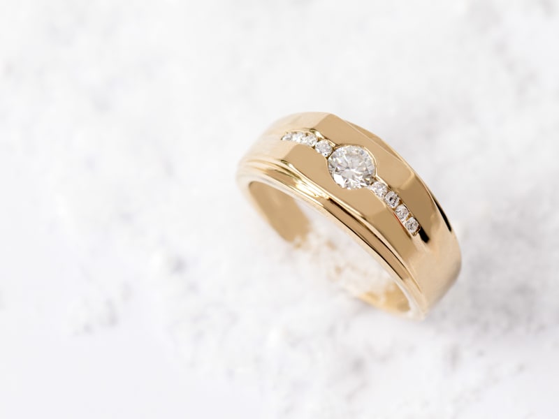 A gold men's ring with a row of diamonds on it 