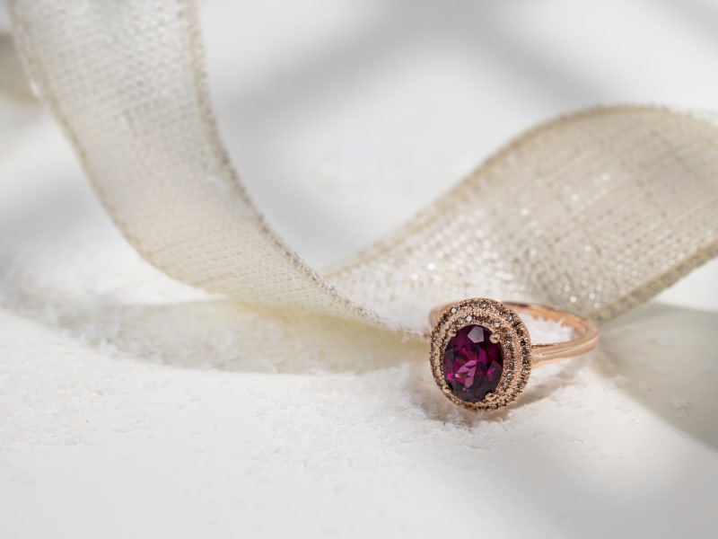 A gold garnet halo ring with a gold ribbon in the background 