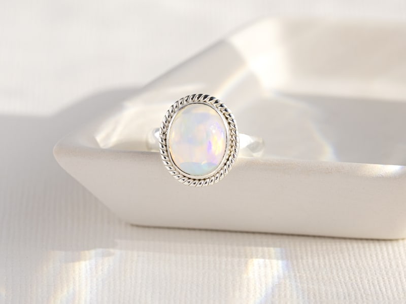 A silver opal ring sitting in a white dish 