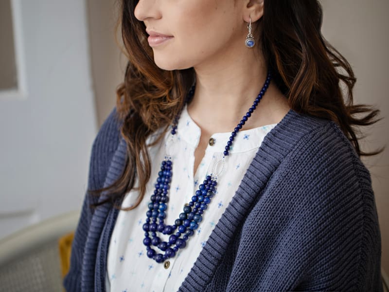 A woman wearing white and blue clothing and a blue lapis lazuli beaded necklace 