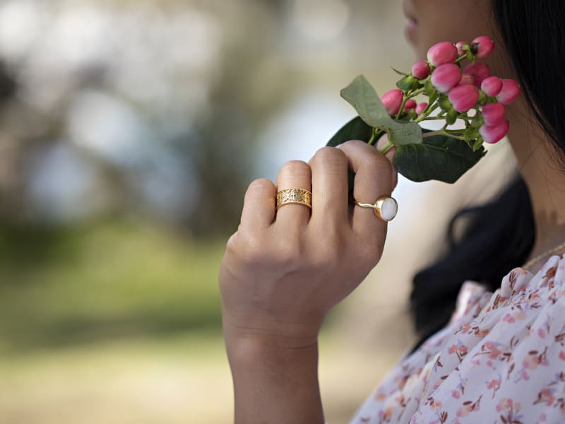 A woman wearing two rings and a necklace, holding a sprig of pink flowers  
