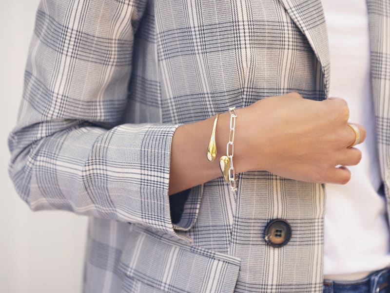 A woman in a gray plaid blazer wearing silver and gold bracelets and a ring 