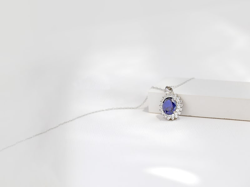 A blue gemstone pendant necklace with a halo of white stones and a silver chain 