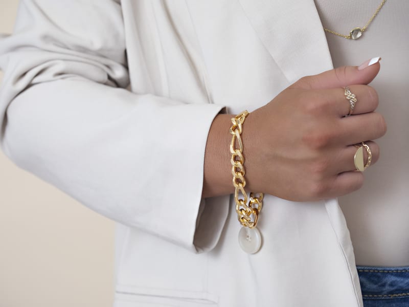 A woman in a white blazer wearing gold bracelets, a necklace and rings 