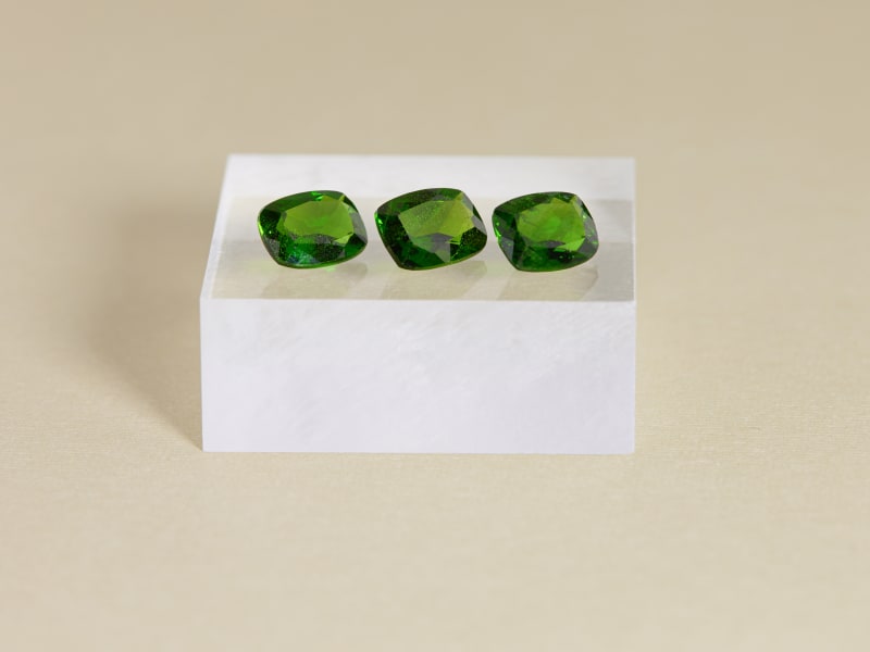 Three loose chrome diopside stones sitting in a row on a white pedestal 