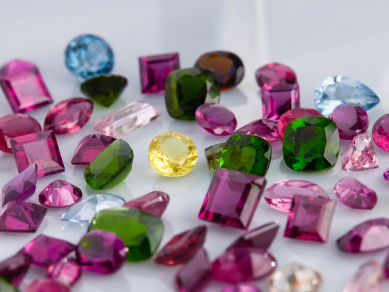 An assortment of chrome diopside stones with other purple, blue, yellow and brown gems 