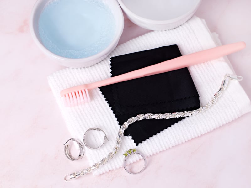 Silver jewelry and cleaning supplies, including a toothbrush, a water bowl, and cloths 