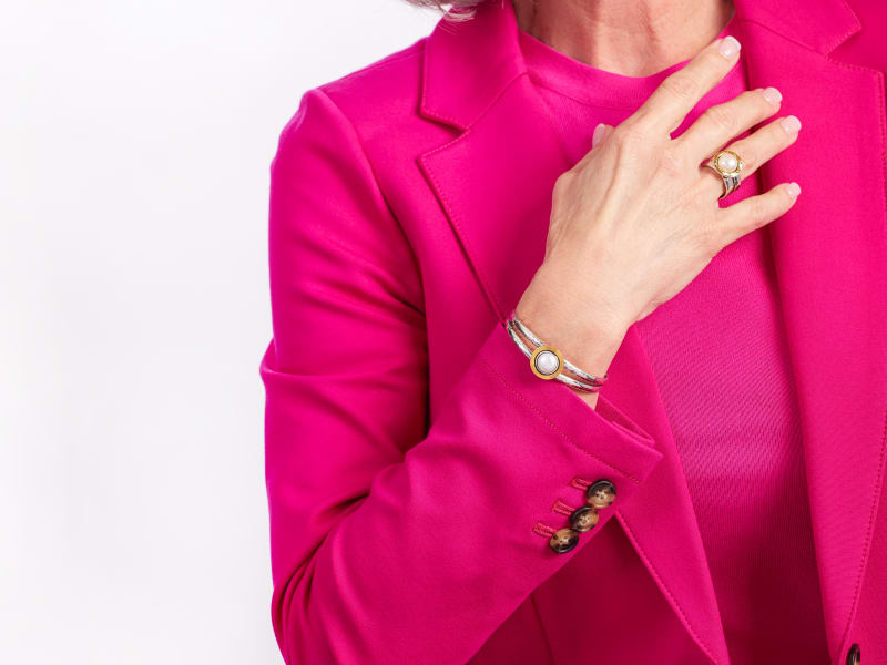 A woman in a magenta suit wearing pearl and gold jewelry 