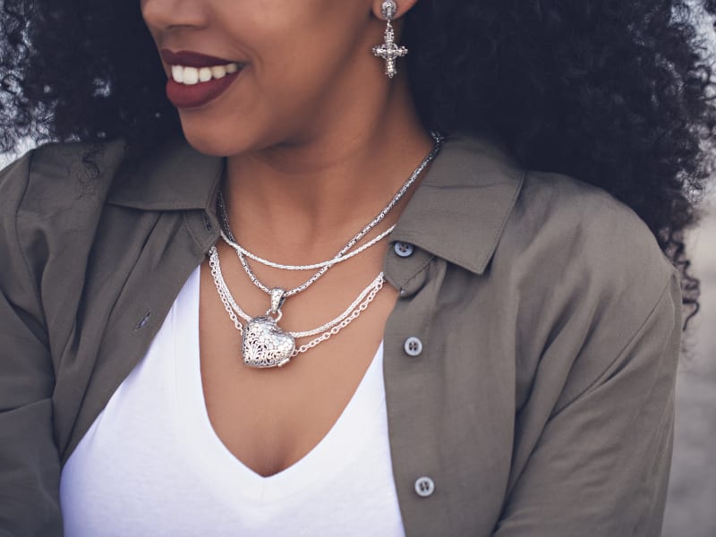 A woman wearing layered silver necklaces and silver cross earrings 