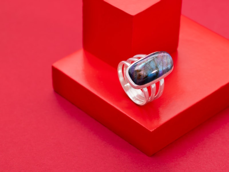 A silver and labradorite ring against a red background 